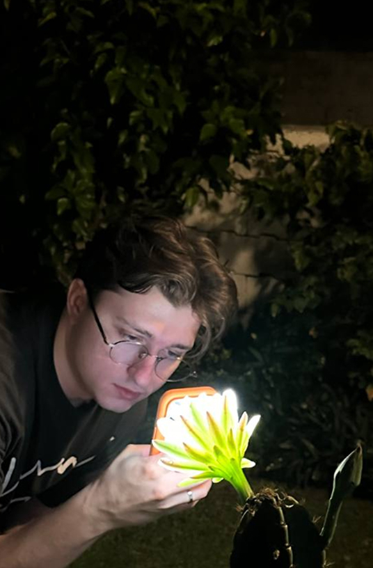 Ilya Marchuk at night, lighting a blooming flower with his phone